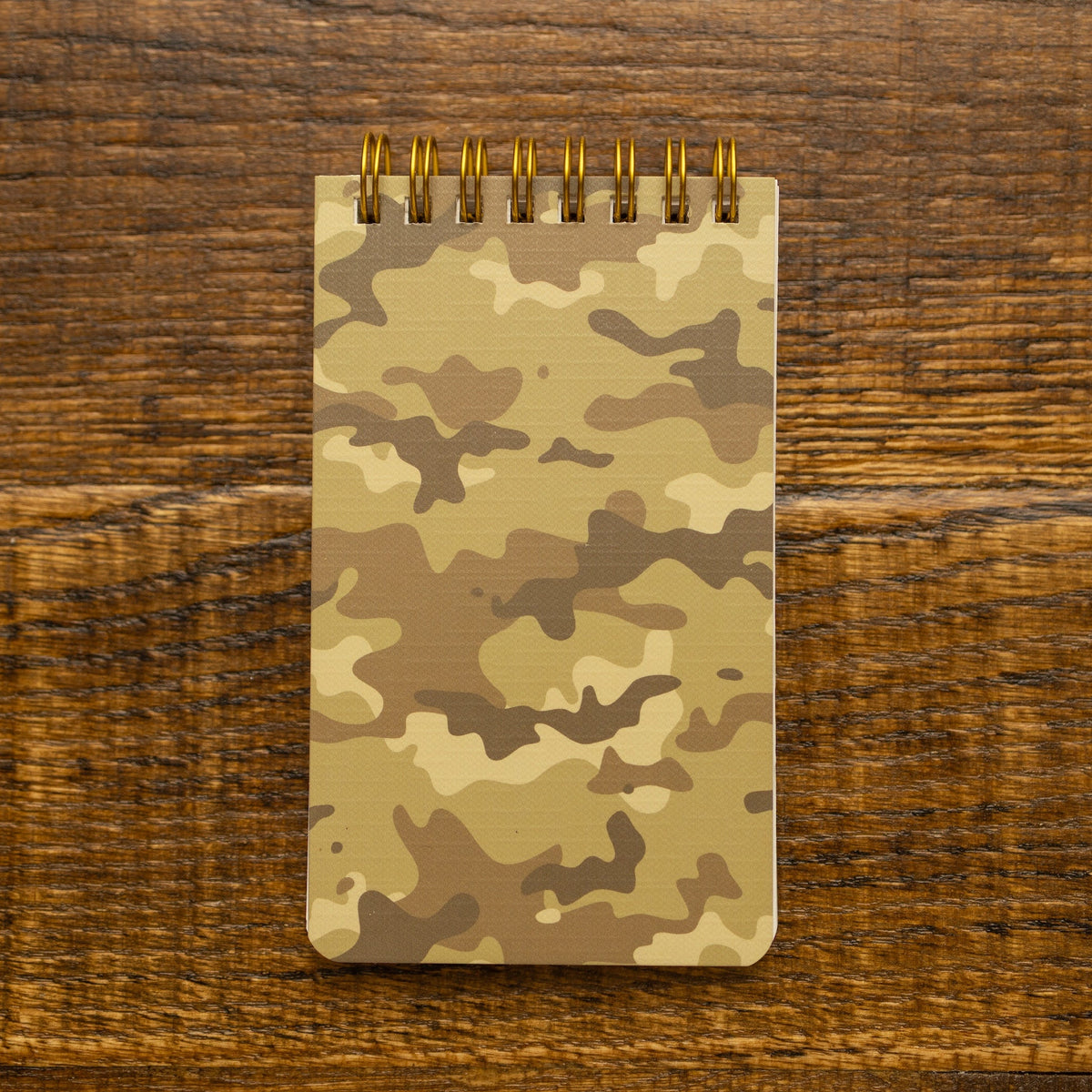 A spiral-bound notepad with a tan and brown camouflage pattern, placed on a dark wood tabletop.