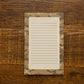 A lined notepad with a camouflage border, placed flat on a rustic wooden surface.