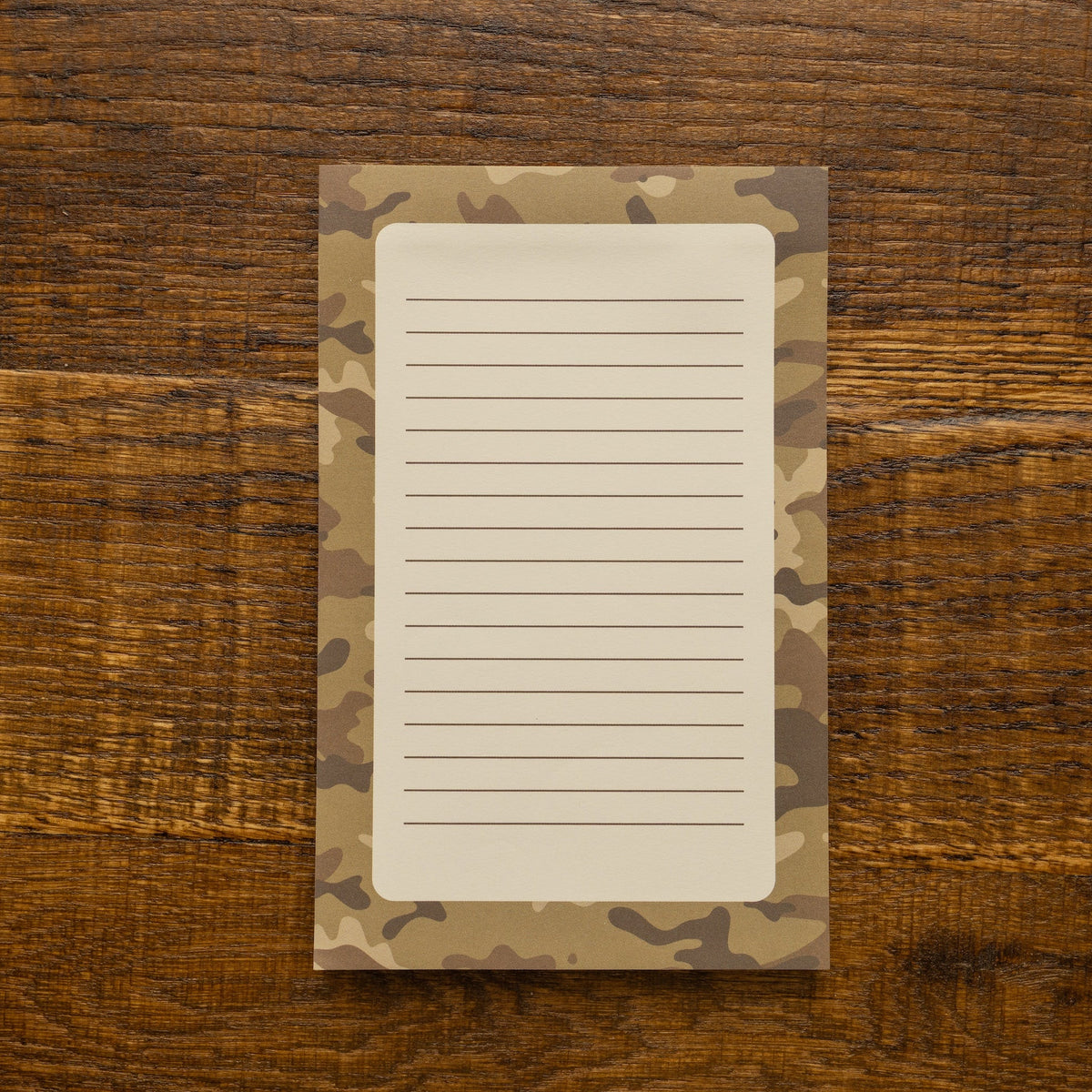 A lined notepad with a camouflage border, placed flat on a rustic wooden surface.