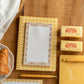 A styled flat-lay of a yellow gingham spiral notebook with a lined paper insert on a wooden tabletop, alongside butter sticks, a pen, another notebook, and a croissant.